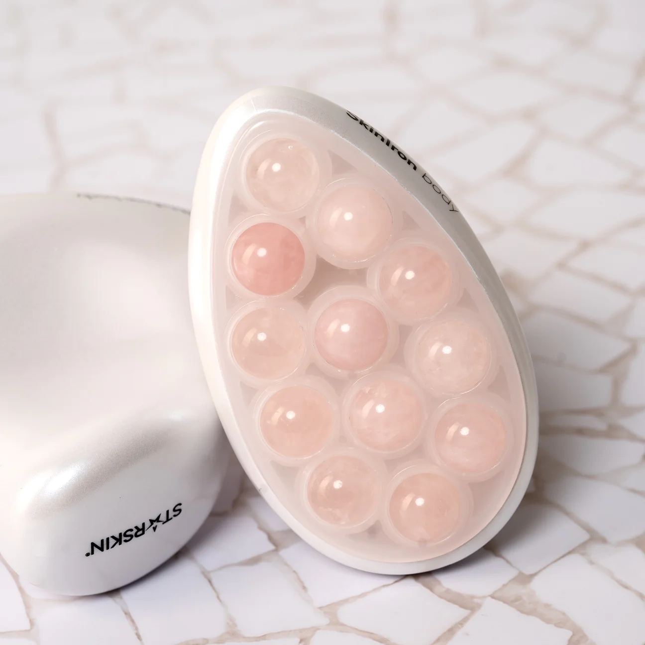 Ein weißes Hautpflegegerät mit mehreren runden, rosafarbenen Kugeln auf einer Marmoroberfläche.
