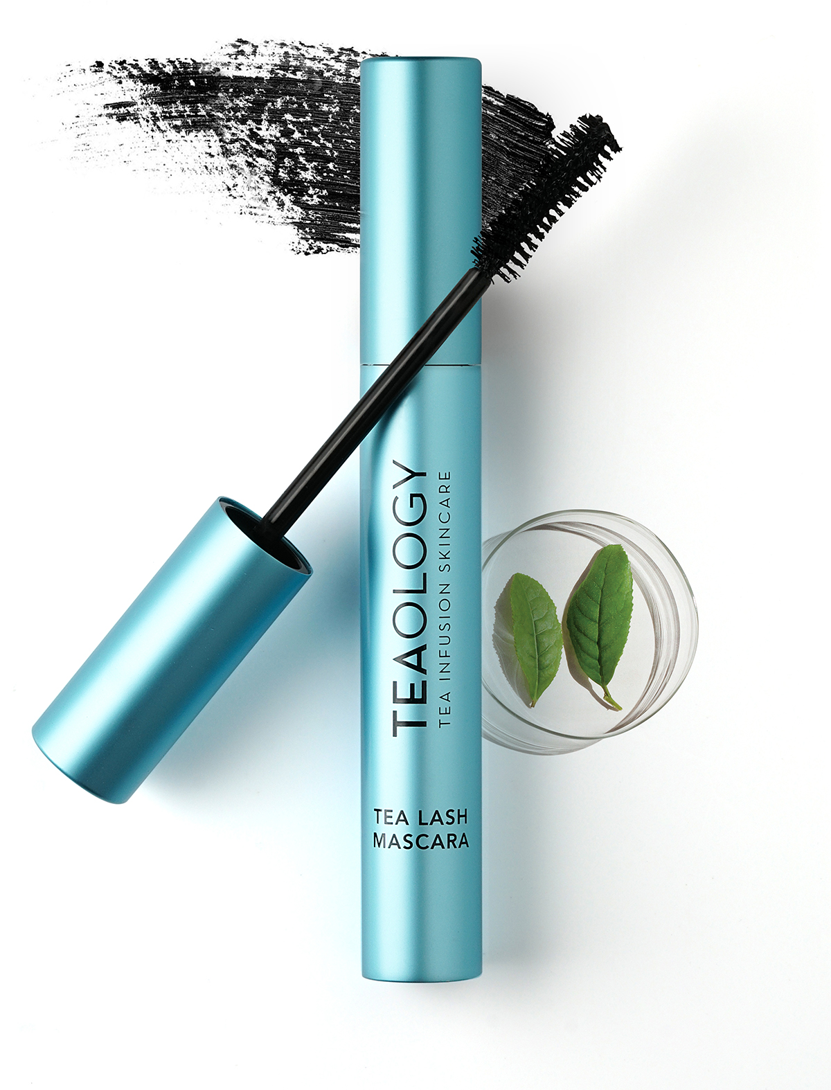 TEAOLOGY Tea Lash Mascara in türkisfarbener Tube, geöffnet, mit Pinsel und Teeblättern im Hintergrund.